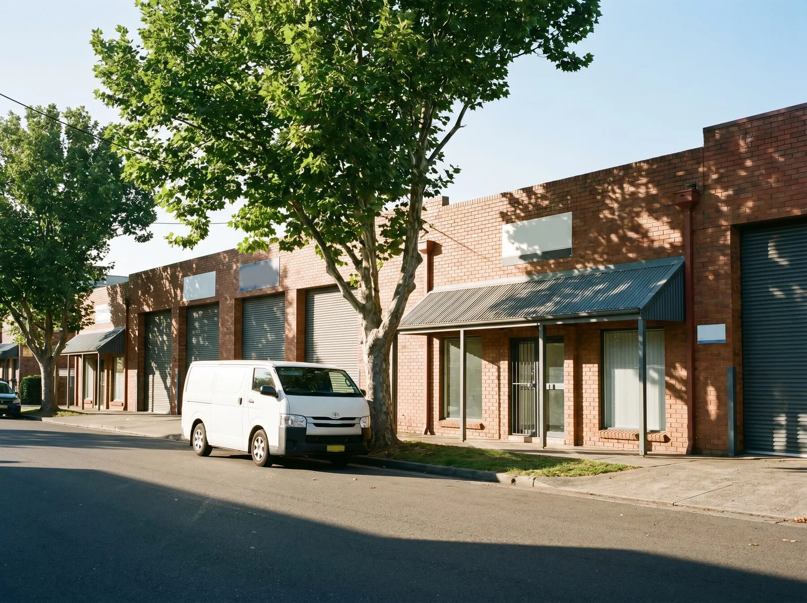 A tidy light-industrial street in Artarmon with brick warehouse units, roller doors and a parked van